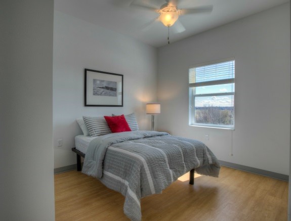 A bedroom from the Redtail Ponds property. The room has a bed against one wall, a window and ceiling fan.