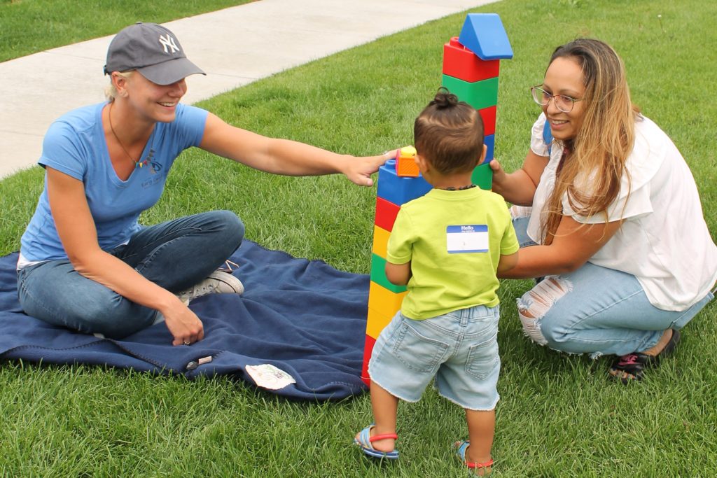 Toddler builds on the grass with teacher and parent