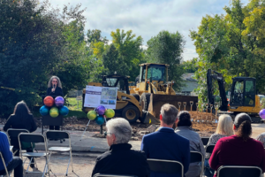 Woman speaks at podium in front of bulldozer