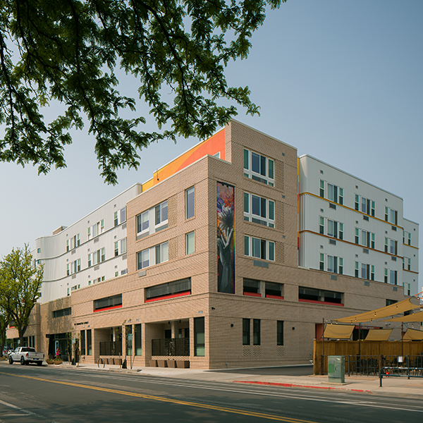 Building with brick and corrugated steel facade featuring mural with a flower and outstretched hand